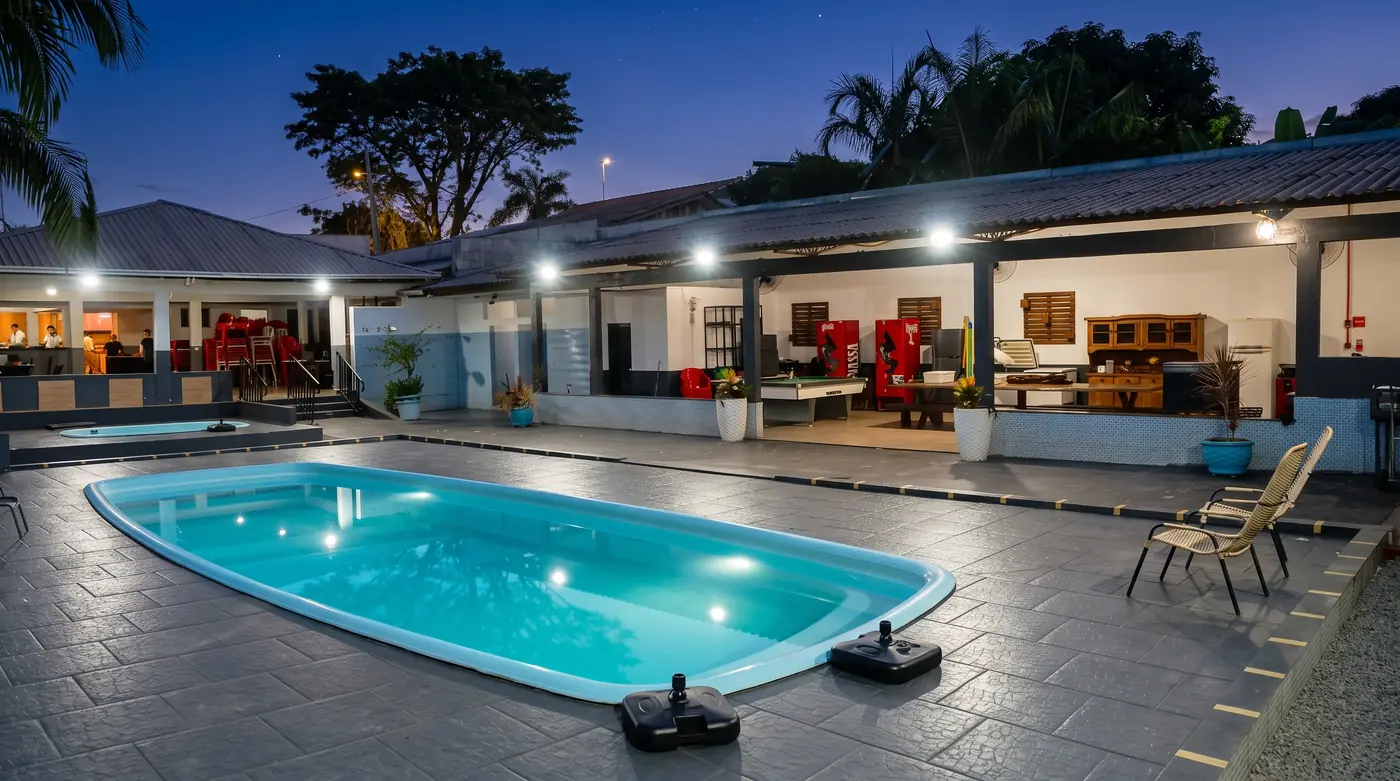 Piscina iluminada à noite com espreguiçadeiras e área coberta ao fundo