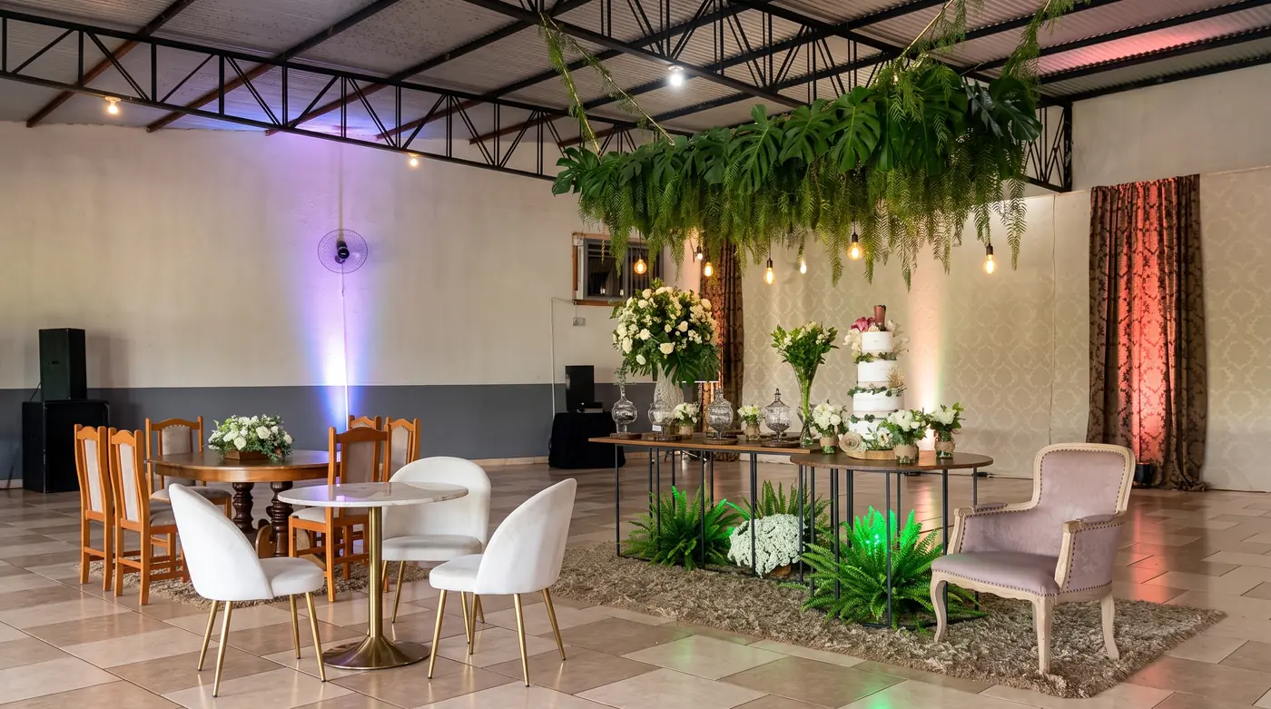 Mesa de bolo decorada com folhagens suspensas, poltronas e mesas de apoio